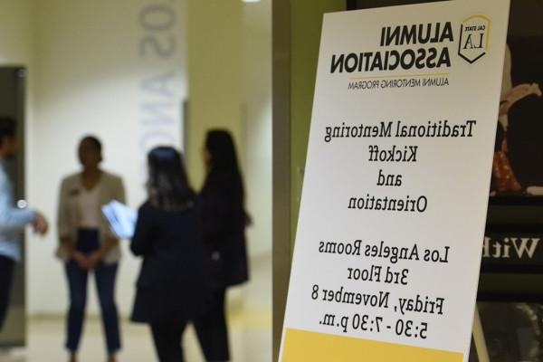 Sign for mentoring orientation with a group of people chatting in the background